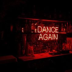 a neon sign that says dance again on the side of a bar with bottles behind it