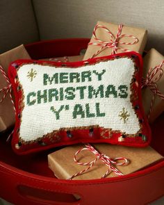 a christmas pillow and some presents in a red basket with ribbon on the bottom that says merry christmas y'all