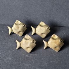 four brass fish shaped knobs on a black surface with one facing the camera and five to the side