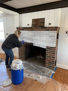 a woman is painting a brick fireplace in the living room