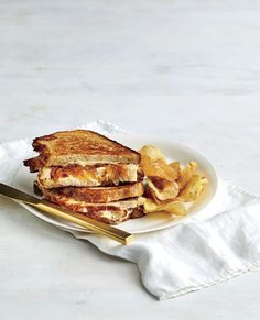 a white plate topped with grilled cheese and french fries next to a gold fork