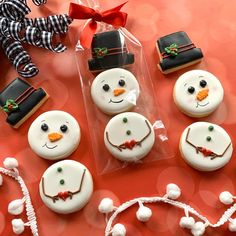 decorated cookies in the shape of snowmen on a red table with candy and decorations