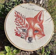 an embroidered fox with blue eyes and red leaves on it's head is sitting in the grass