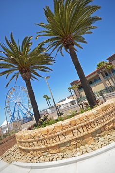 two palm trees in front of a sign and ferris wheel at the county fairgrounds