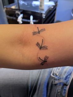 a woman's arm with three small dragonflies on the back of her arm