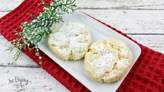 two powdered sugar cookies on a white plate with a red napkin and green sprig