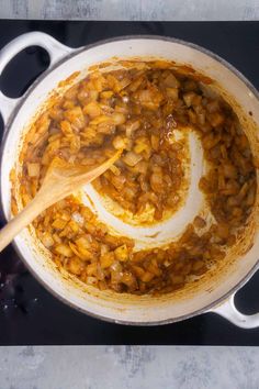 a large pot filled with food on top of a stovetop next to a wooden spoon