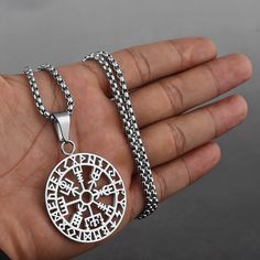 a hand holding a silver pendant with an intricate design