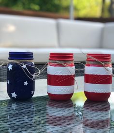 three patriotic mason jars tied with twine and sitting on a glass table outside in the sun