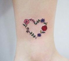 a small heart shaped tattoo with flowers on the side of the foot and behind it is a rose