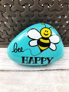 a painted rock with a bee on it and the words be happy written on it