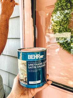 a person holding a can of paint in front of a door with the words behr painted on it