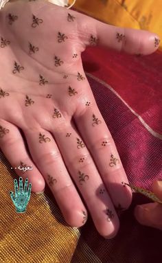 a person's hand with small tattoos on it and flowers in the middle of their fingers