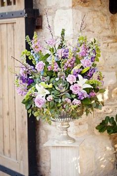 a vase filled with purple and white flowers sitting on top of a stone floor next to a wooden door