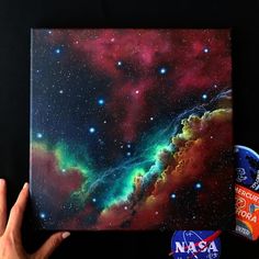 a hand is holding up a painting that looks like an image of the stars in space