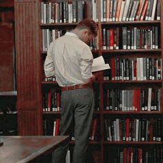 a man standing in front of a book shelf filled with books and looking at it