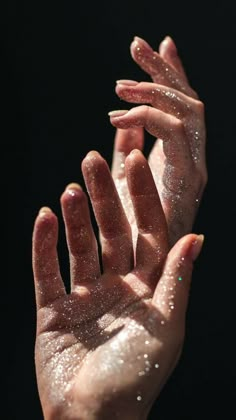 two hands are covered with glitter against a black background