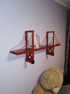 a teddy bear is sitting in front of a wall shelf with a bridge on it