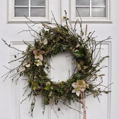 a wreath on the front door of a house with flowers hanging from it's side