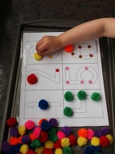 a toddler is playing with pom poms in a tray on the floor