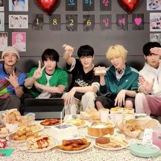 group of young men sitting around a table with food on it and balloons in the background