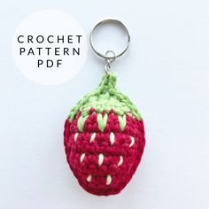 a crocheted strawberry keychain hanging from a metal hook on a white surface