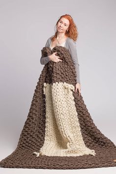 a woman is holding a large knitted blanket