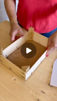 a person standing over a wooden table with a box on it's side and an object in the middle