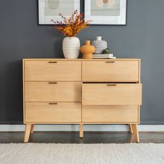 a wooden dresser with two vases on top of it next to a painting and rug