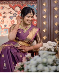 a woman in a purple and gold sari sitting down with her hands on her face