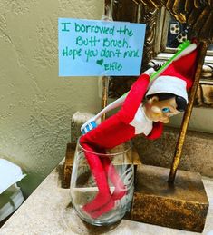 an elf is sitting in a glass with a sign on it