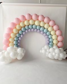 a rainbow balloon arch with pastel colors and white balloons in the shape of clouds