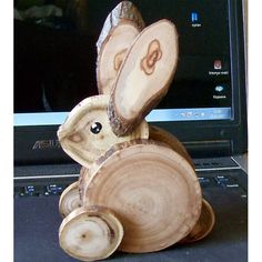 a small wooden bunny sitting on top of a laptop computer next to a tree stump