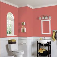 a white toilet sitting next to a sink under a window in a bathroom with pink walls