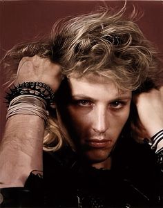 a man with long blonde hair and bracelets on his arm posing for a photo