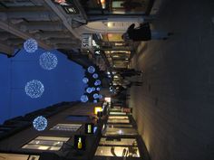 people walking down the street at night with christmas lights hanging from the buildings above them