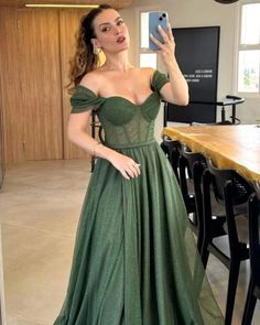 a woman in a green dress taking a selfie with her cell phone while standing next to a table