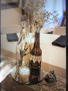 two bottles with flowers and candles on a table