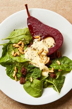 a white plate topped with spinach and beets covered in cheese dressing on top of a bed of leafy greens