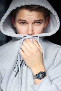 a young man wearing a gray hoodie with his hands on his mouth while looking at the camera