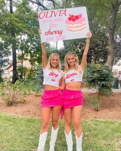 two women in short skirts hold up a sign that says ouva you are the cherry pie