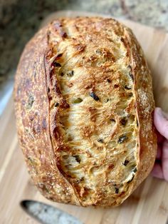 a person holding a loaf of bread on top of a wooden cutting board