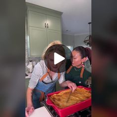 two women in the kitchen preparing food on top of a red baking pan and one woman is pointing at it