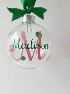 a personalized glass ornament hanging on a wall with a green ribbon and bow