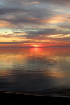 the sun is setting over the ocean with clouds in the sky and reflecting on the water