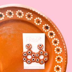 a pair of earrings sitting on top of a brown plate next to a pink background