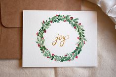 a card with the word joy written in gold on it and a christmas wreath design