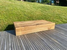 a wooden box sitting on top of a wooden deck next to a green field and trees