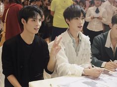 two young men sitting at a table in front of a group of people with papers