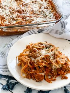 a white plate topped with pasta and meat covered in sauce next to a casserole dish